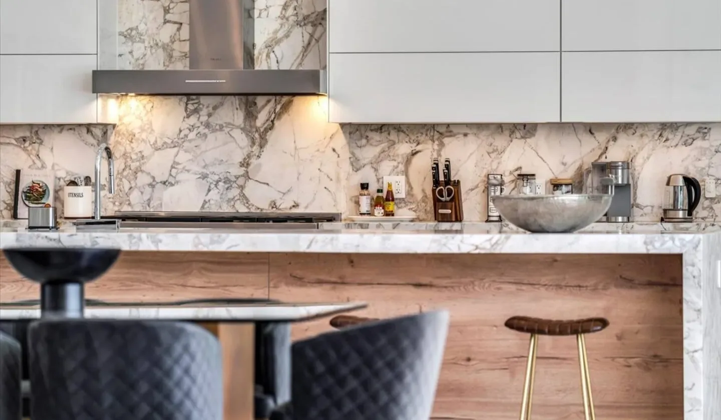A modern kitchen with a marble-patterned backsplash and a counter with seating.