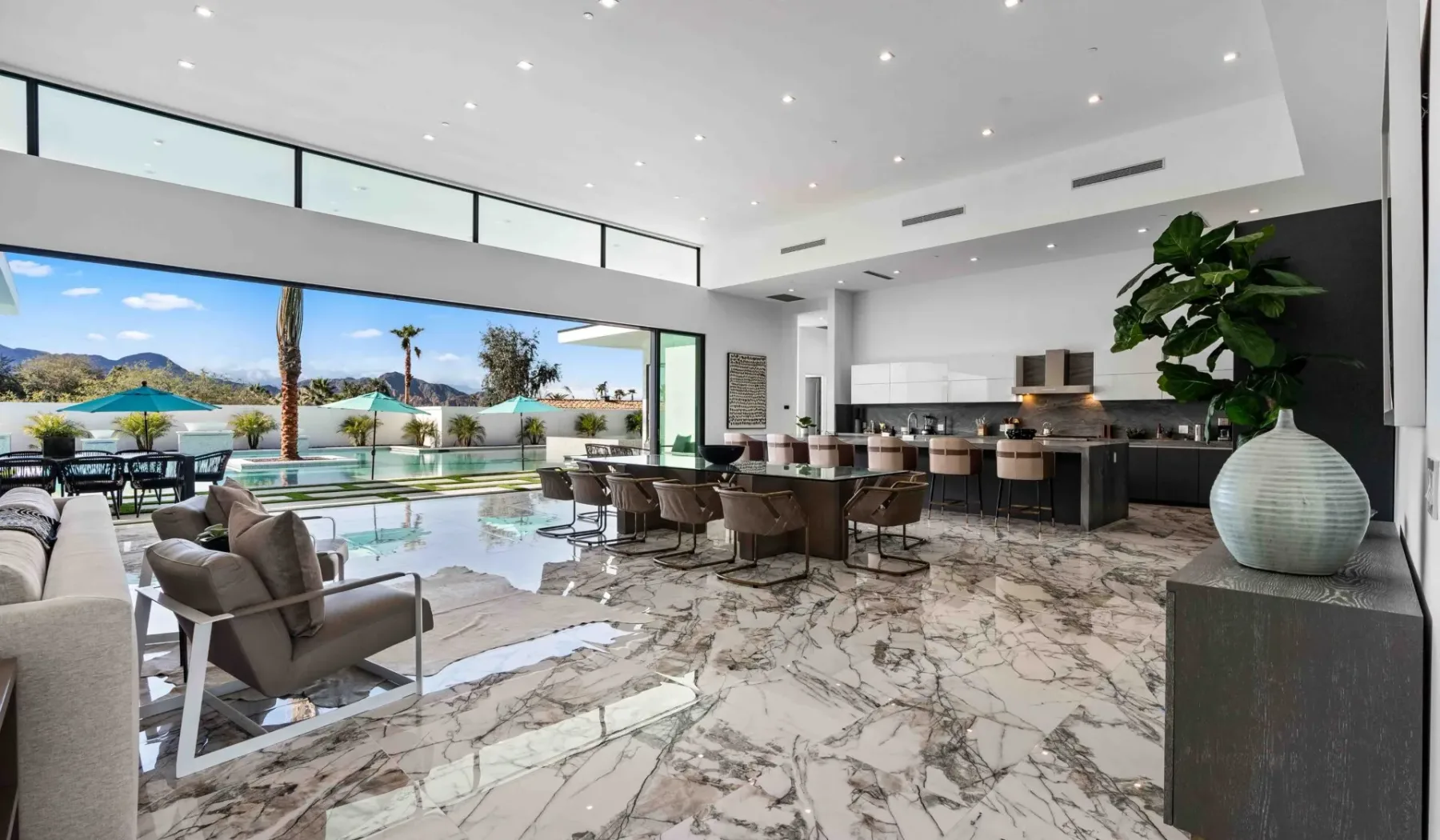 An open-plan dining and kitchen area overlooks a swimming pool through wide glass doors.