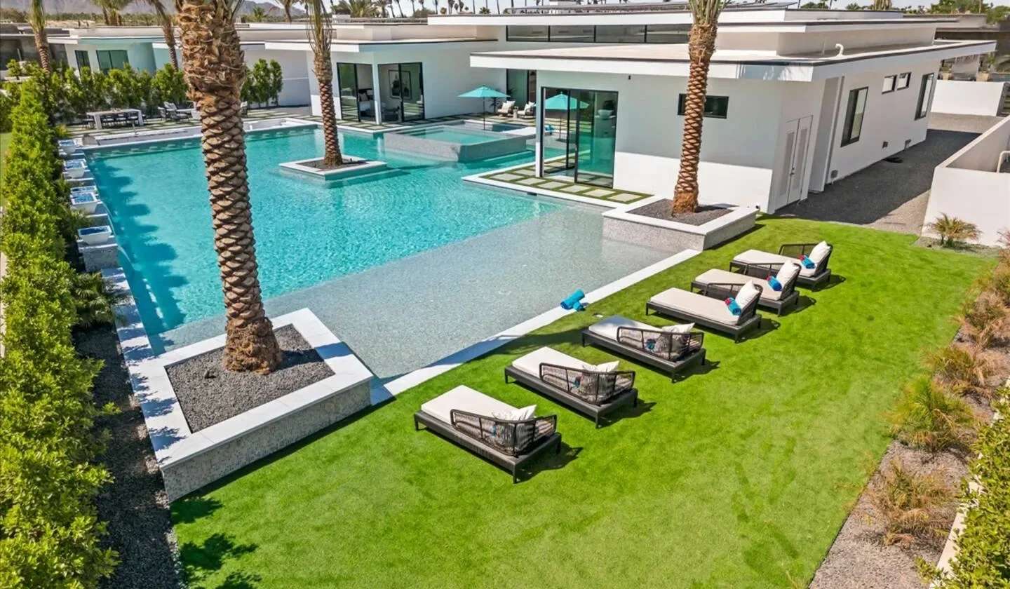 A modern house beside a swimming pool, with lounge seating on the lawn.
