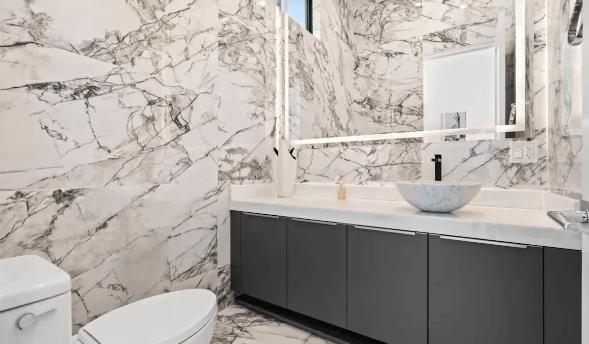 A bathroom with a dark vanity, vessel sink, and marble-patterned walls.