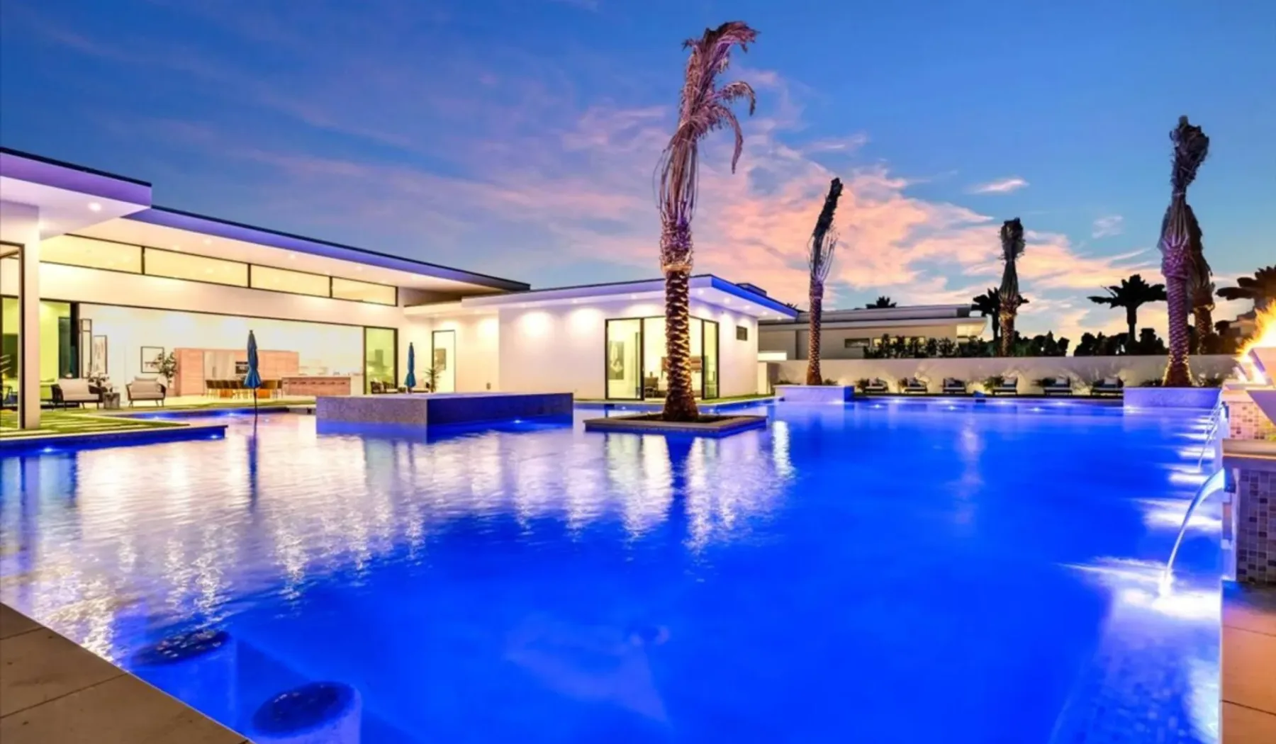 A large blue swimming pool beside a modern building at sunset.