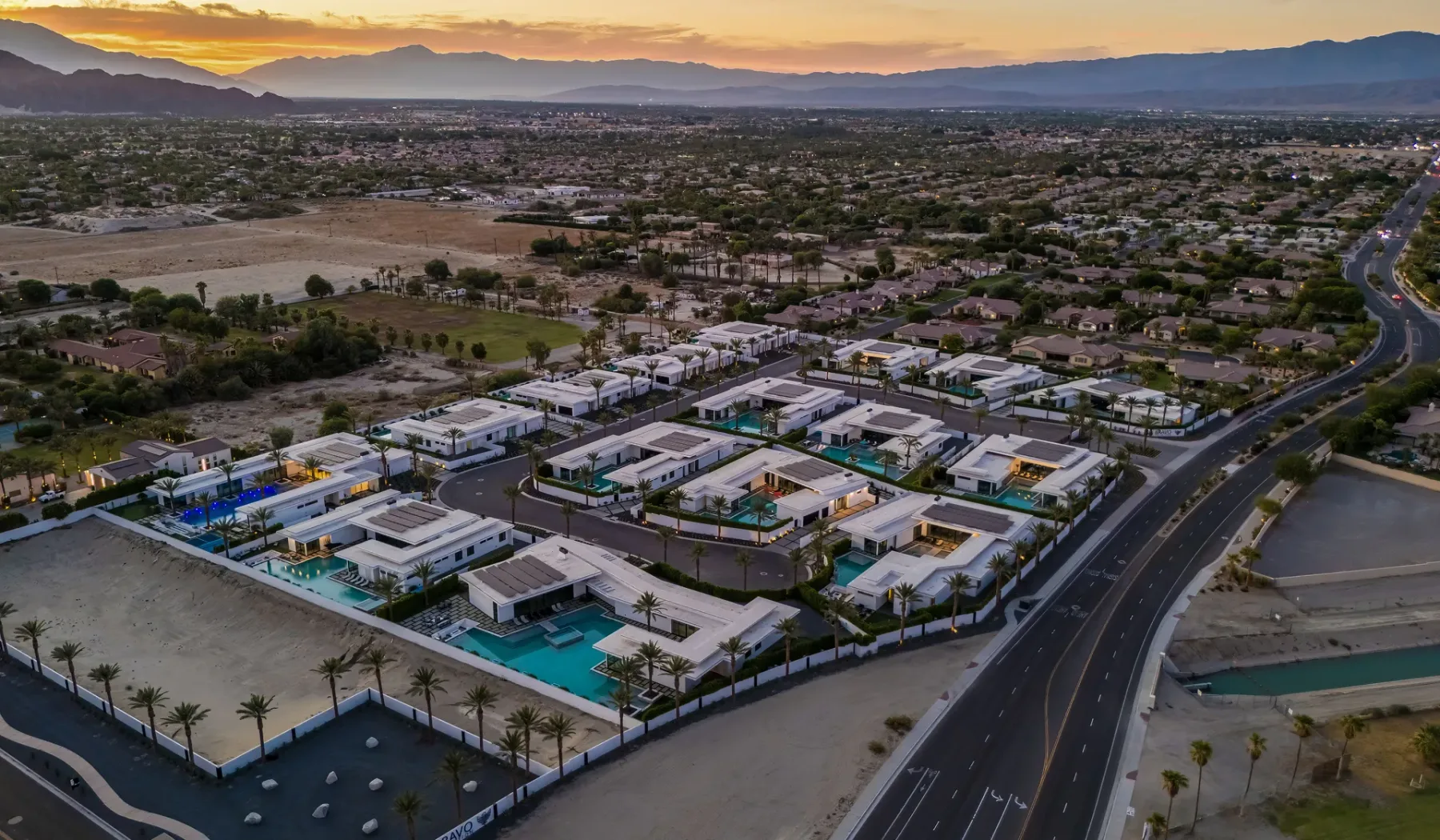 An aerial view of a residential community with homes and pools at sunset.