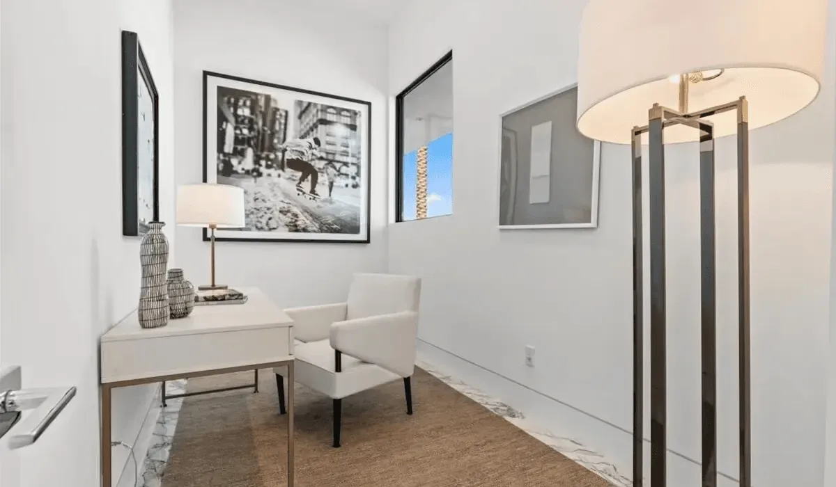A bright sitting area with a desk, armchair, and framed wall art.