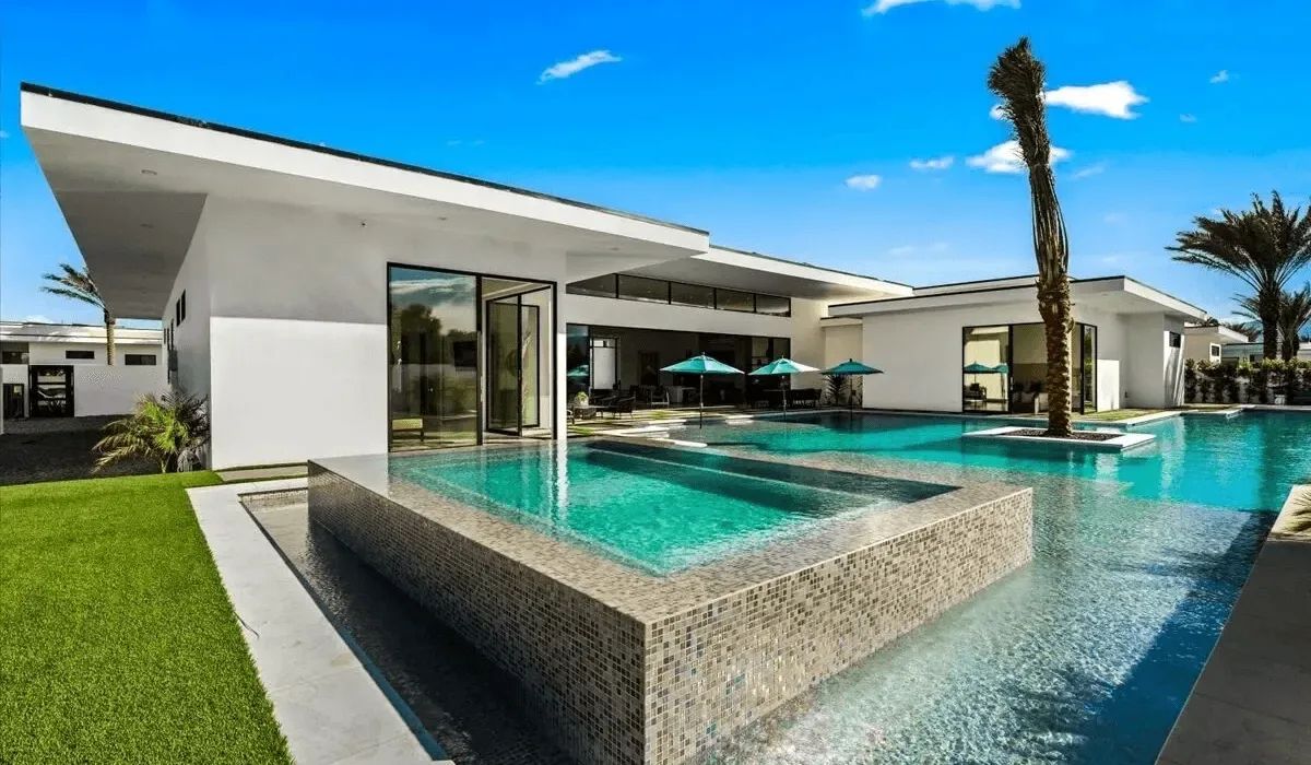 A modern white building overlooks a turquoise pool with a raised square section.