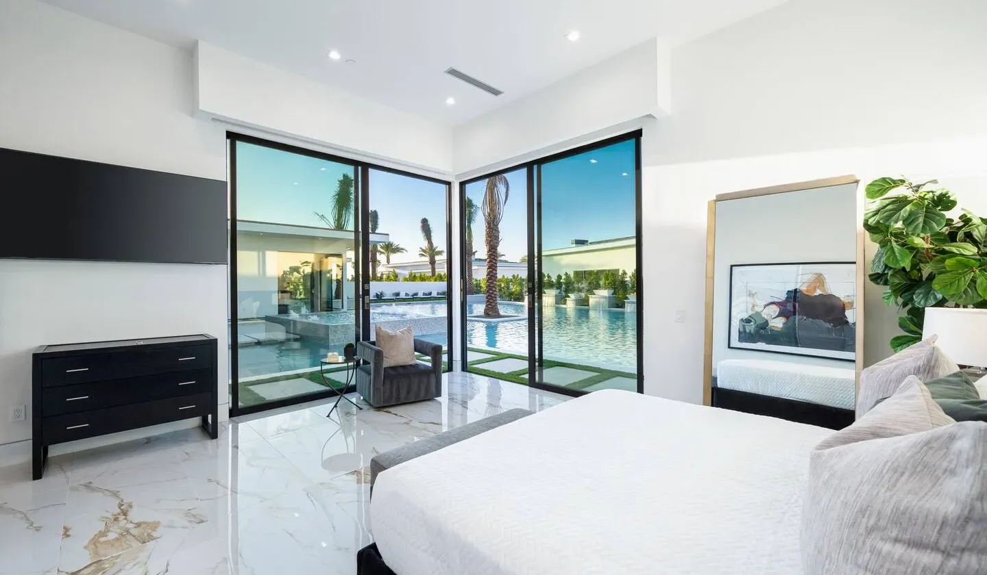 A bright bedroom with a bed and large glass doors overlooking a pool.
