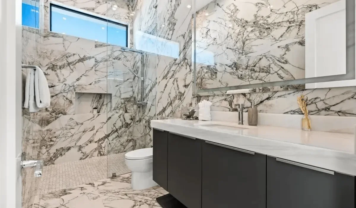 A marble bathroom with a glass shower, toilet, and dark vanity.