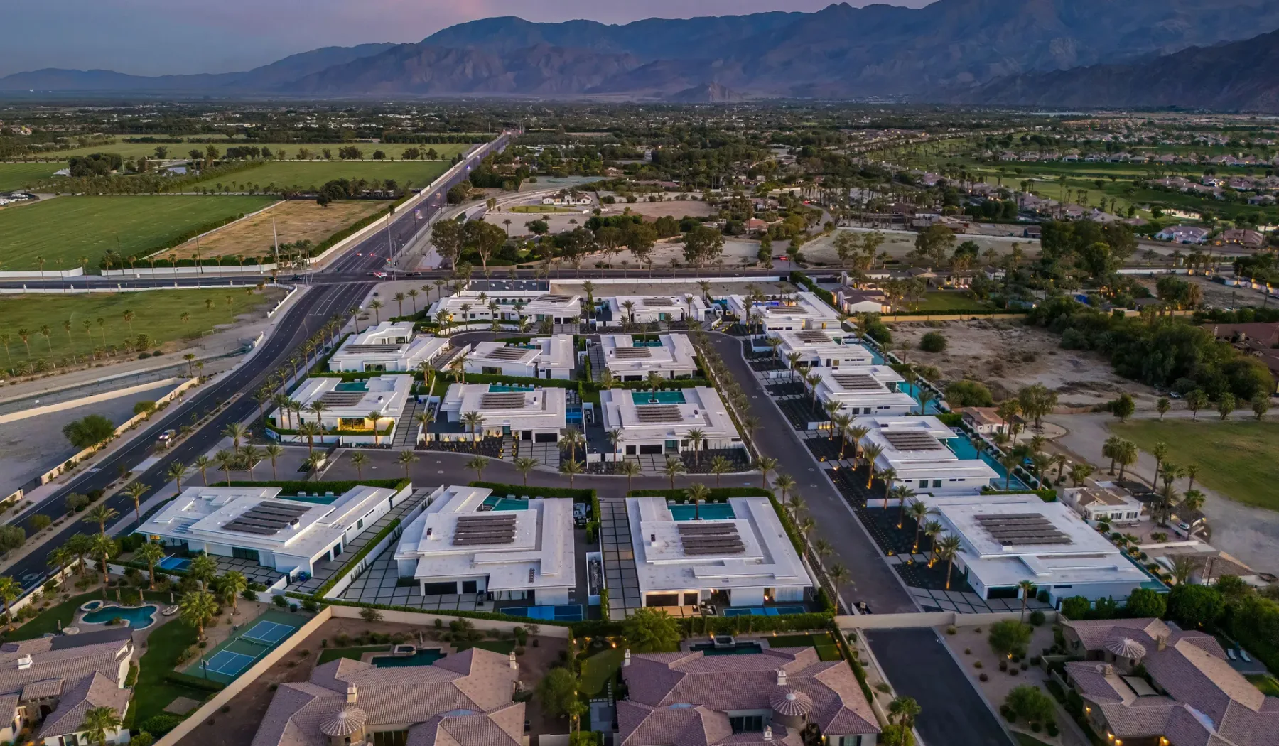 An aerial view of a commercial complex beside roads and green fields, with mountains in the distance.