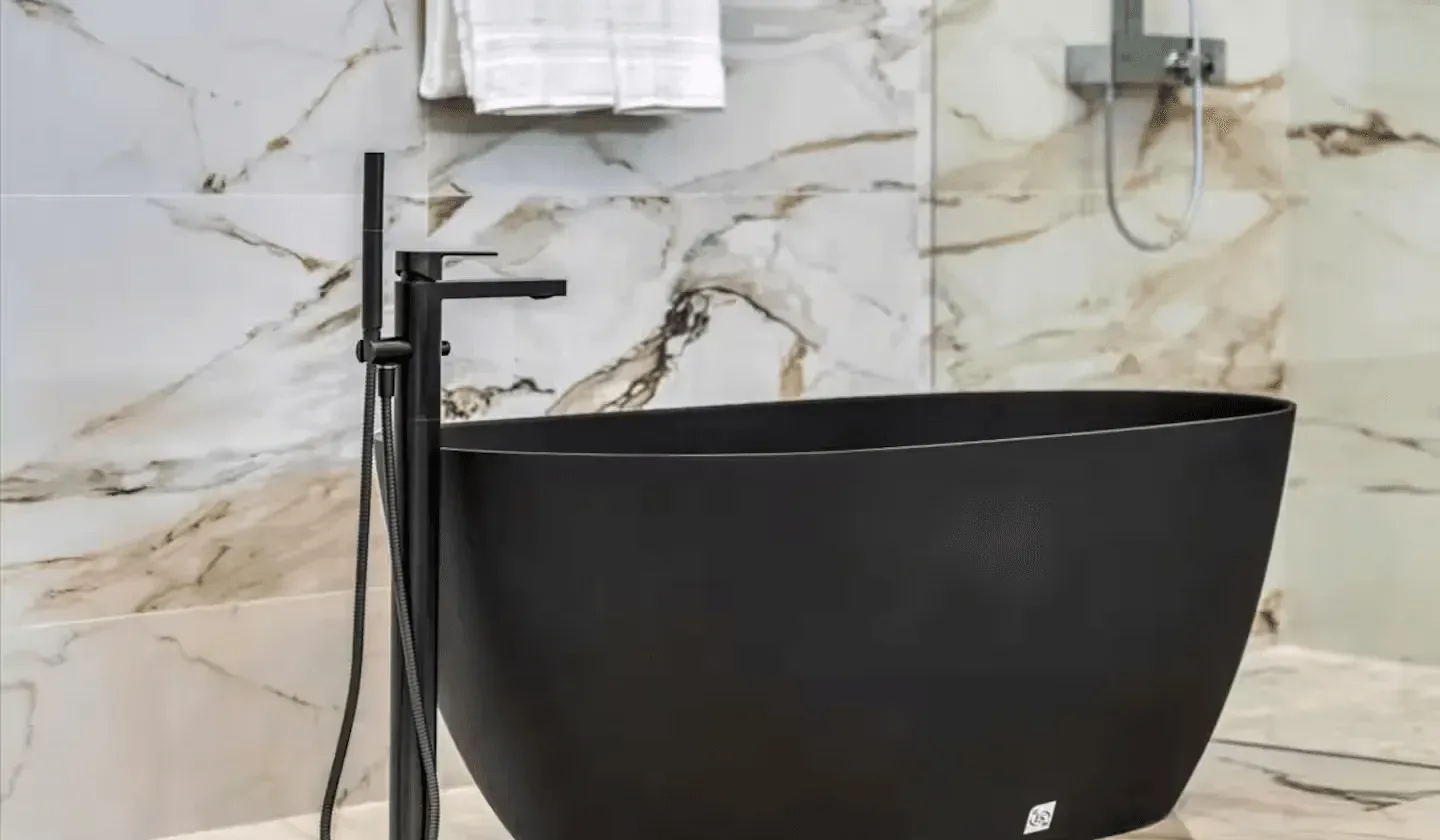 A freestanding bathtub stands against a marble-patterned bathroom wall.