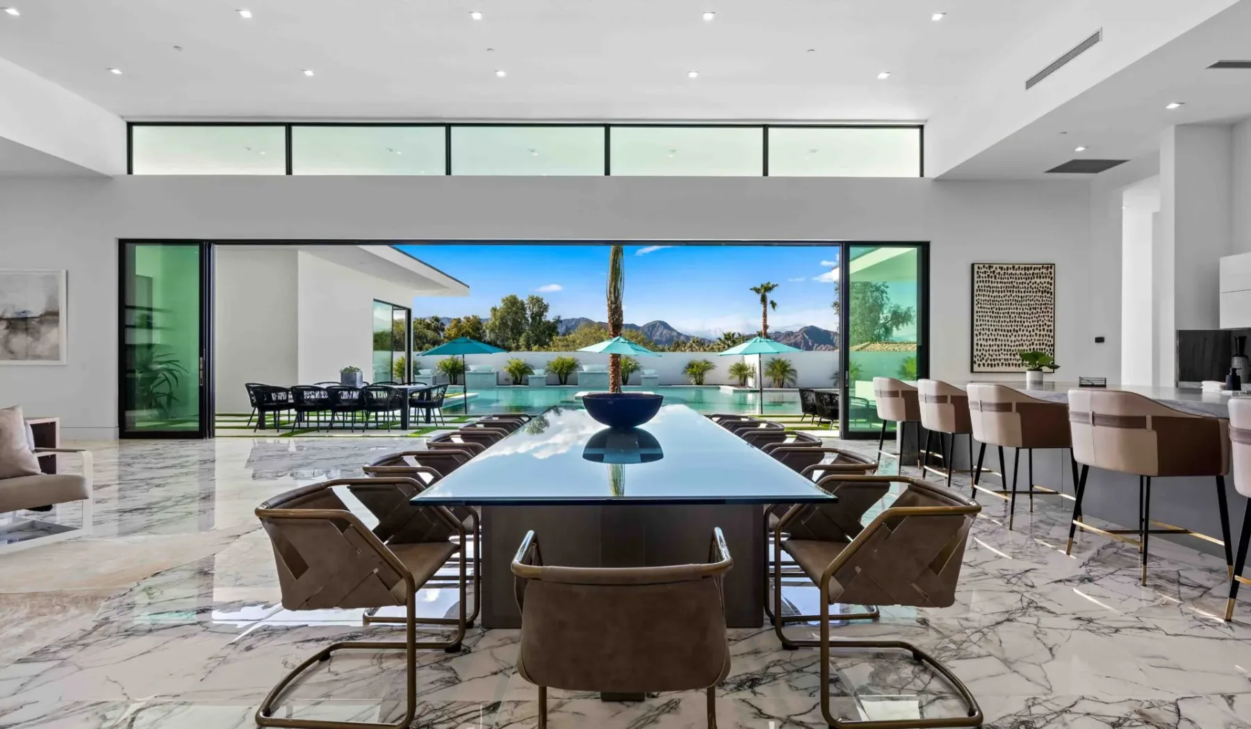 A bright dining area opens onto a patio with a pool and mountain views.