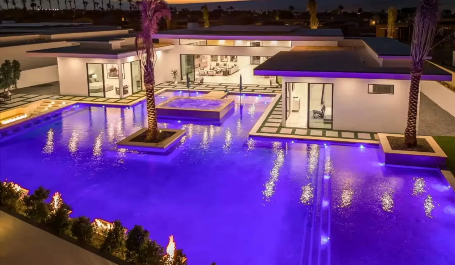 A brightly lit swimming pool surrounds a modern building at night.