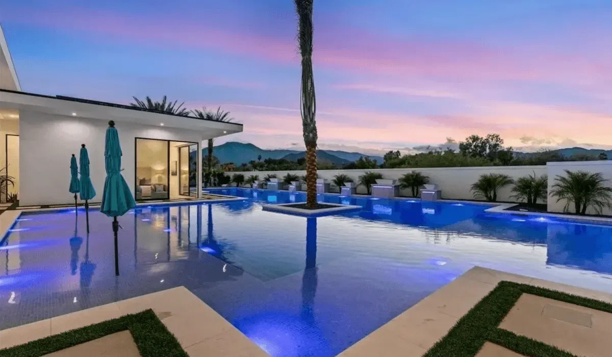 Modern house and illuminated swimming pool beneath a colorful evening sky.