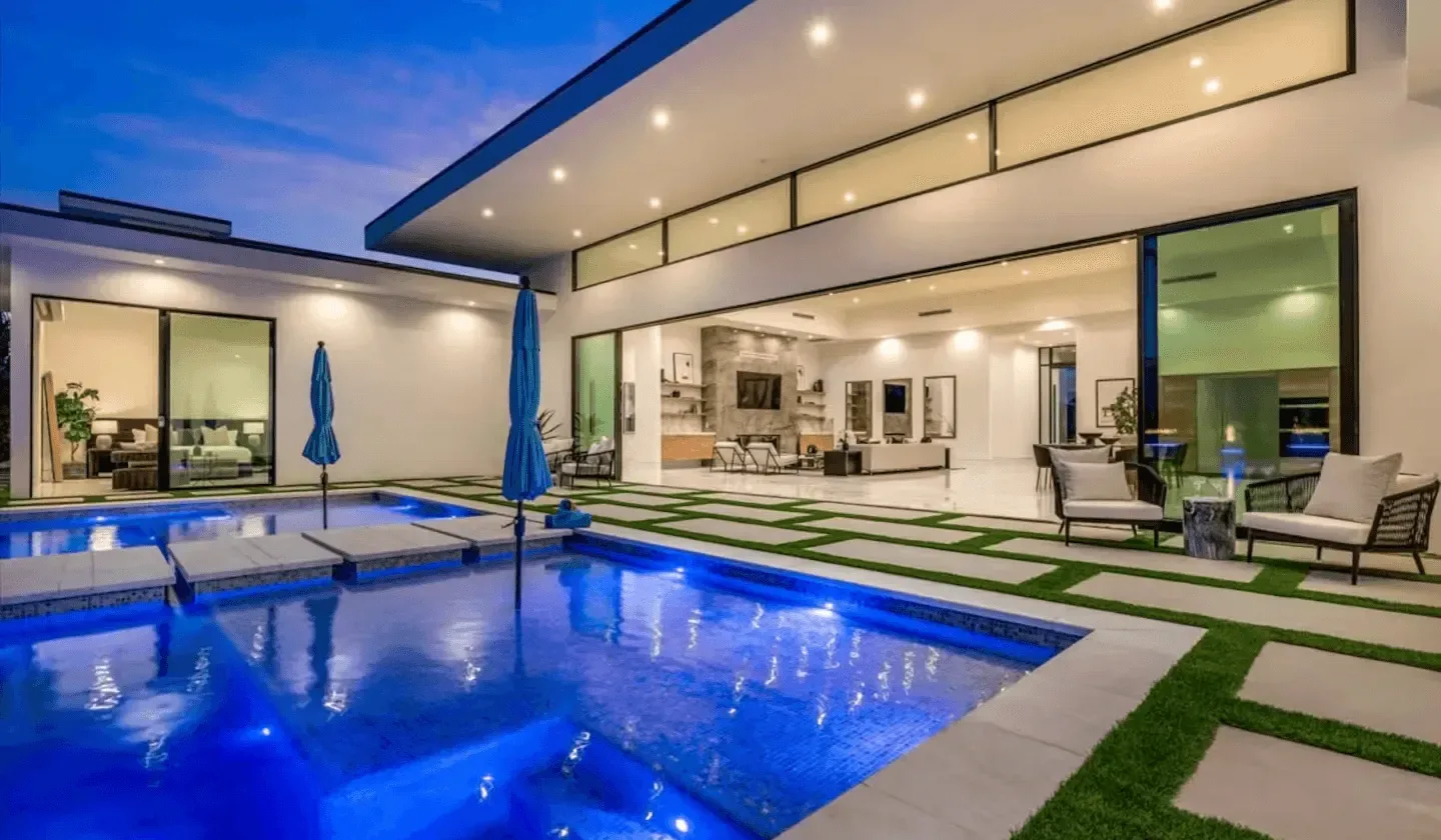 A modern home opens onto a blue swimming pool and outdoor seating.