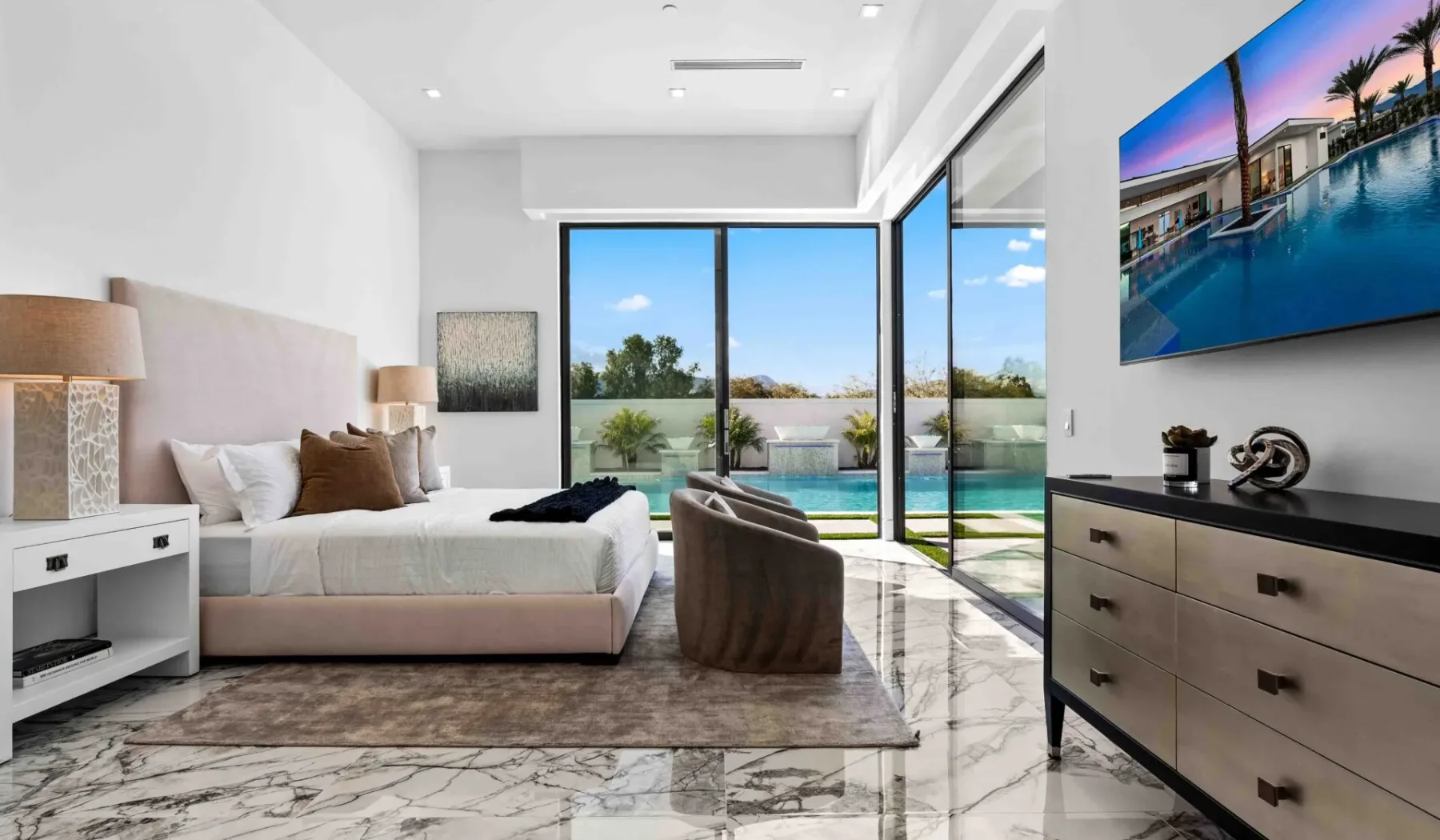 A bright bedroom with a bed beside floor-to-ceiling windows overlooking a pool.