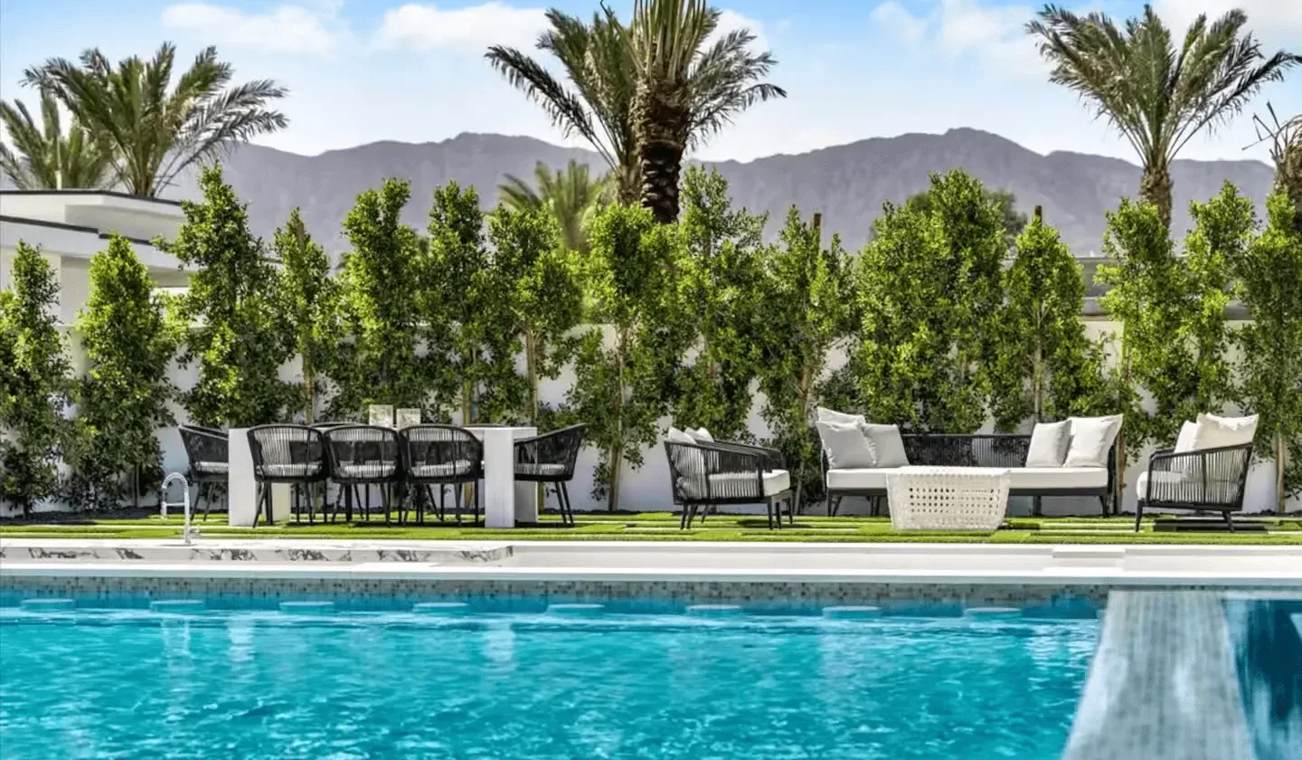 An outdoor pool bordered by leafy greenery and patio seating.