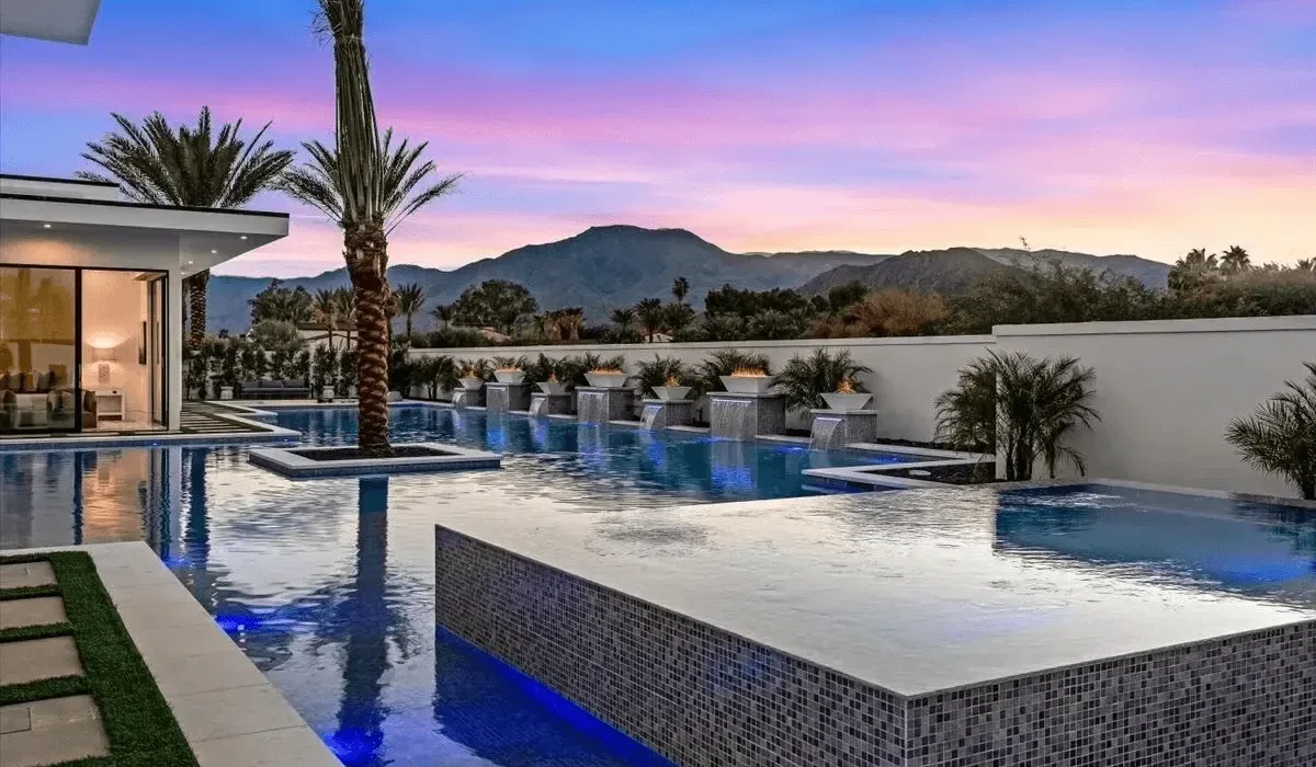 An outdoor swimming pool reflects the colorful evening sky beside a modern building.