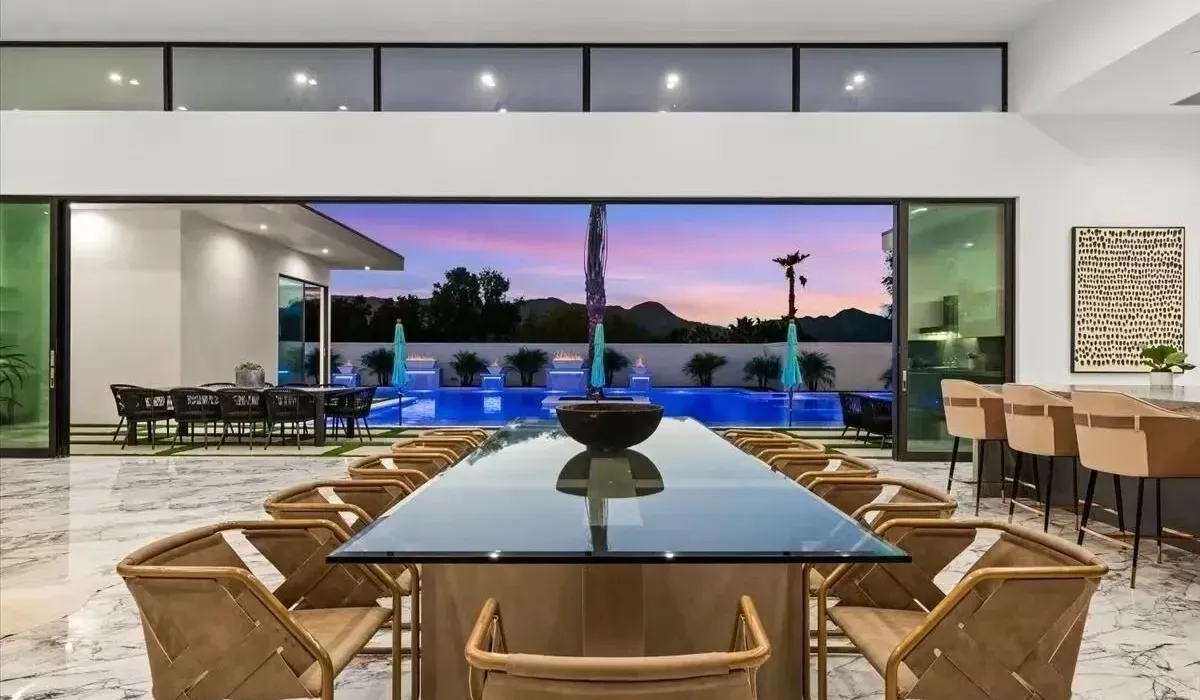 A dining area opens onto a pool, with a long table in the foreground.