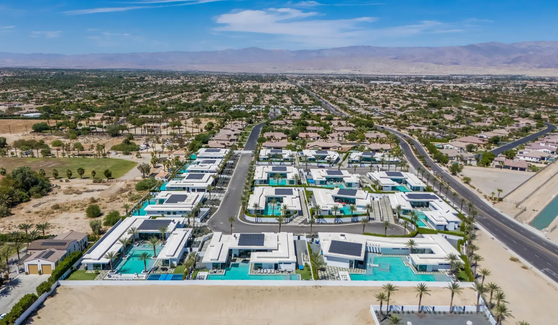 An aerial view of a residential neighborhood with homes, pools, and distant mountains.