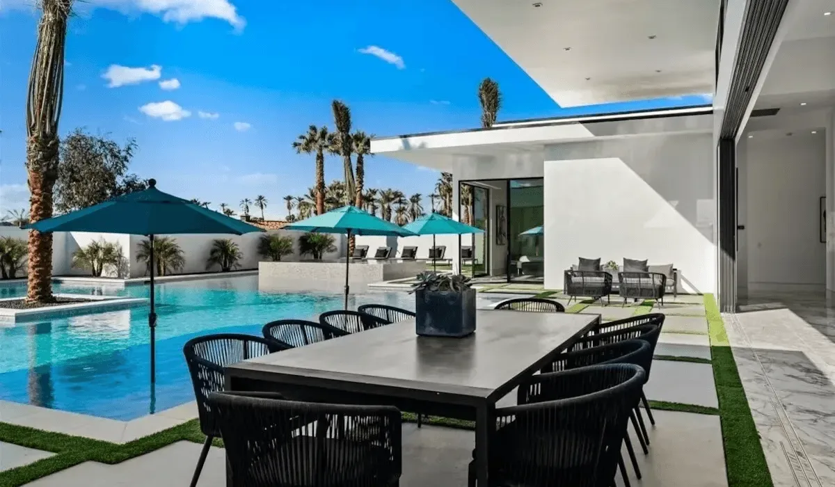 A modern outdoor dining area beside a swimming pool with shaded seating.