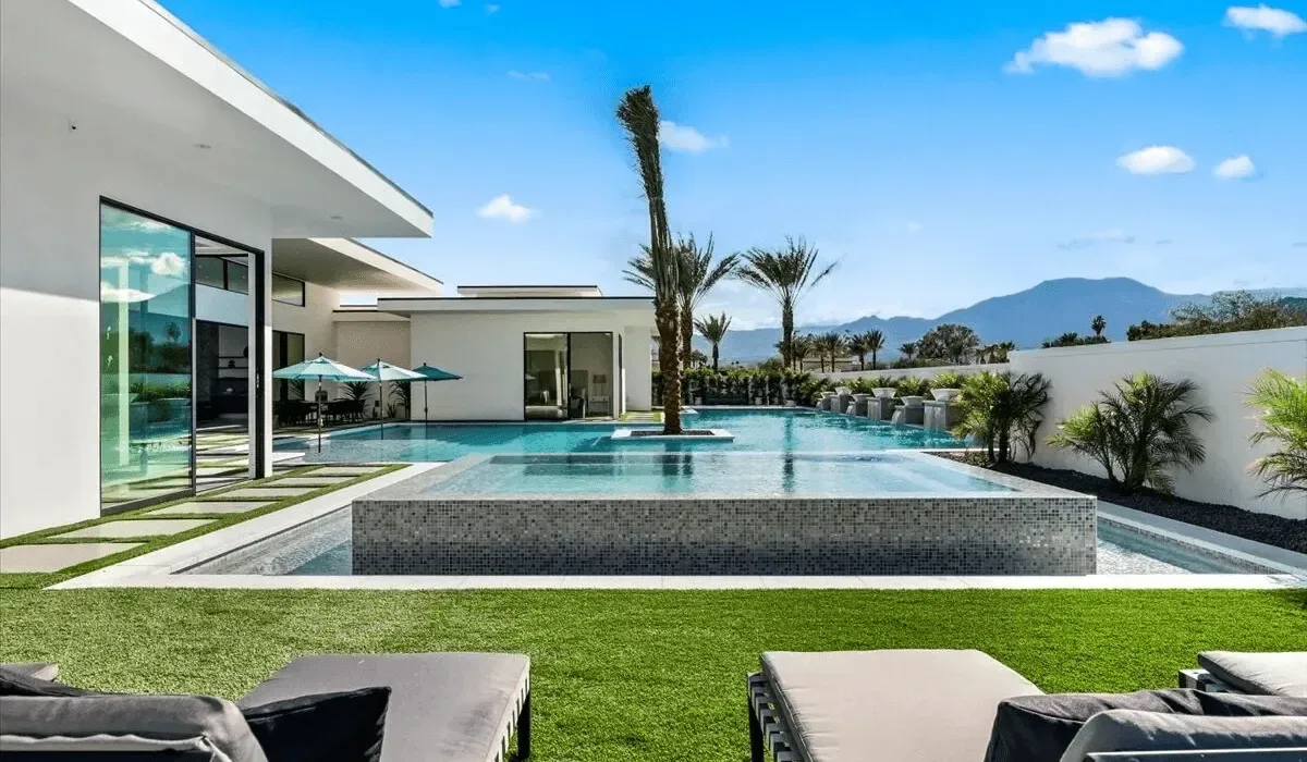 A modern house opens onto a swimming pool, with lawn and mountains beyond.