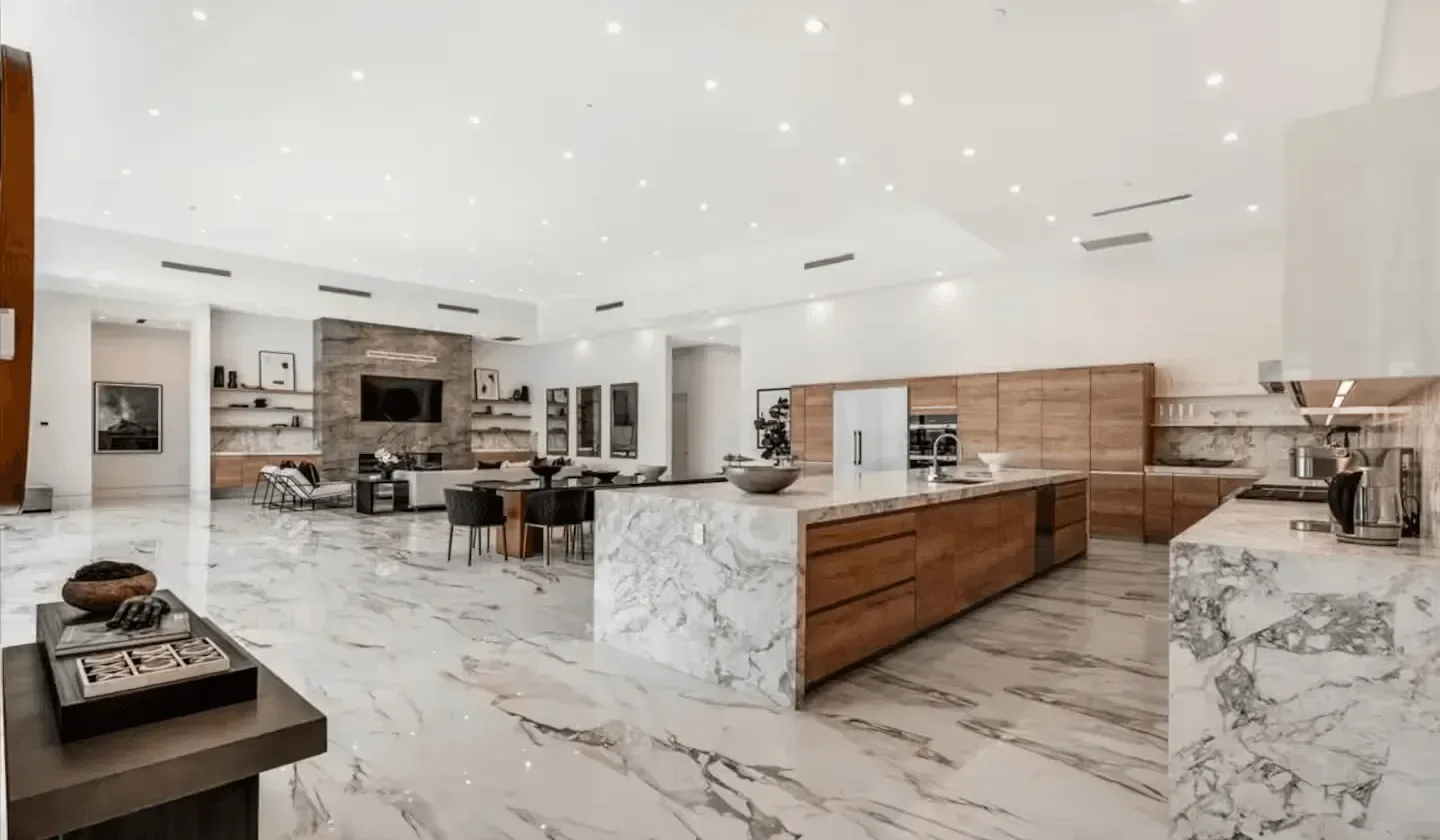 A spacious modern kitchen with a large marble island and wood cabinetry.