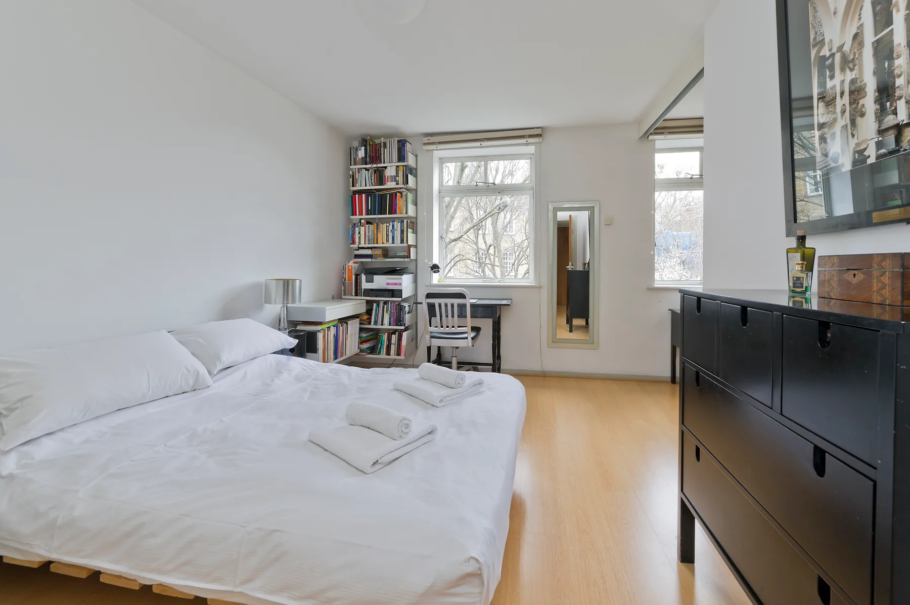 Un dormitorio luminoso con una cama, un escritorio y ventanas altas.