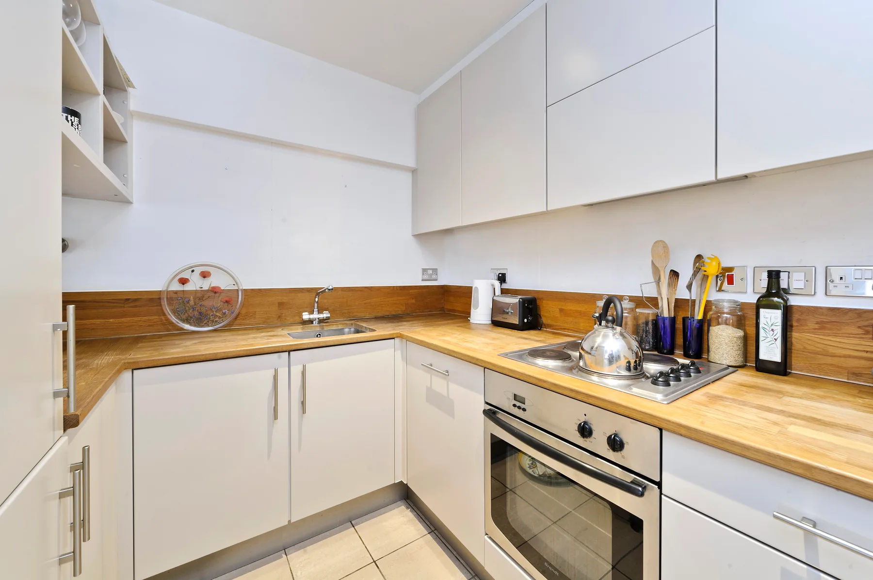 A compact kitchen with pale cabinets, wooden counters, and a built-in oven.