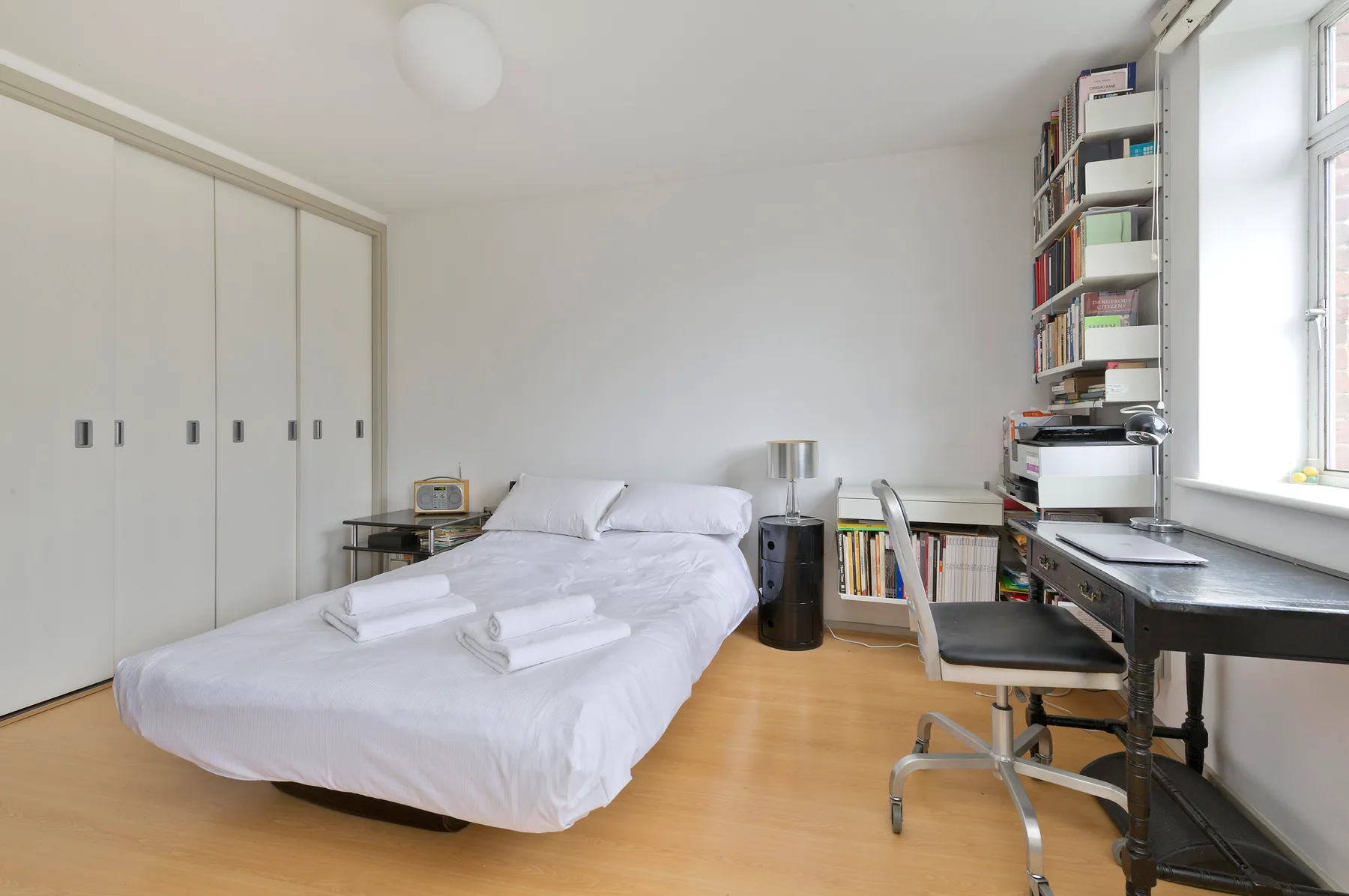 Un dormitorio luminoso con una cama bien tendida y un escritorio junto a la ventana.