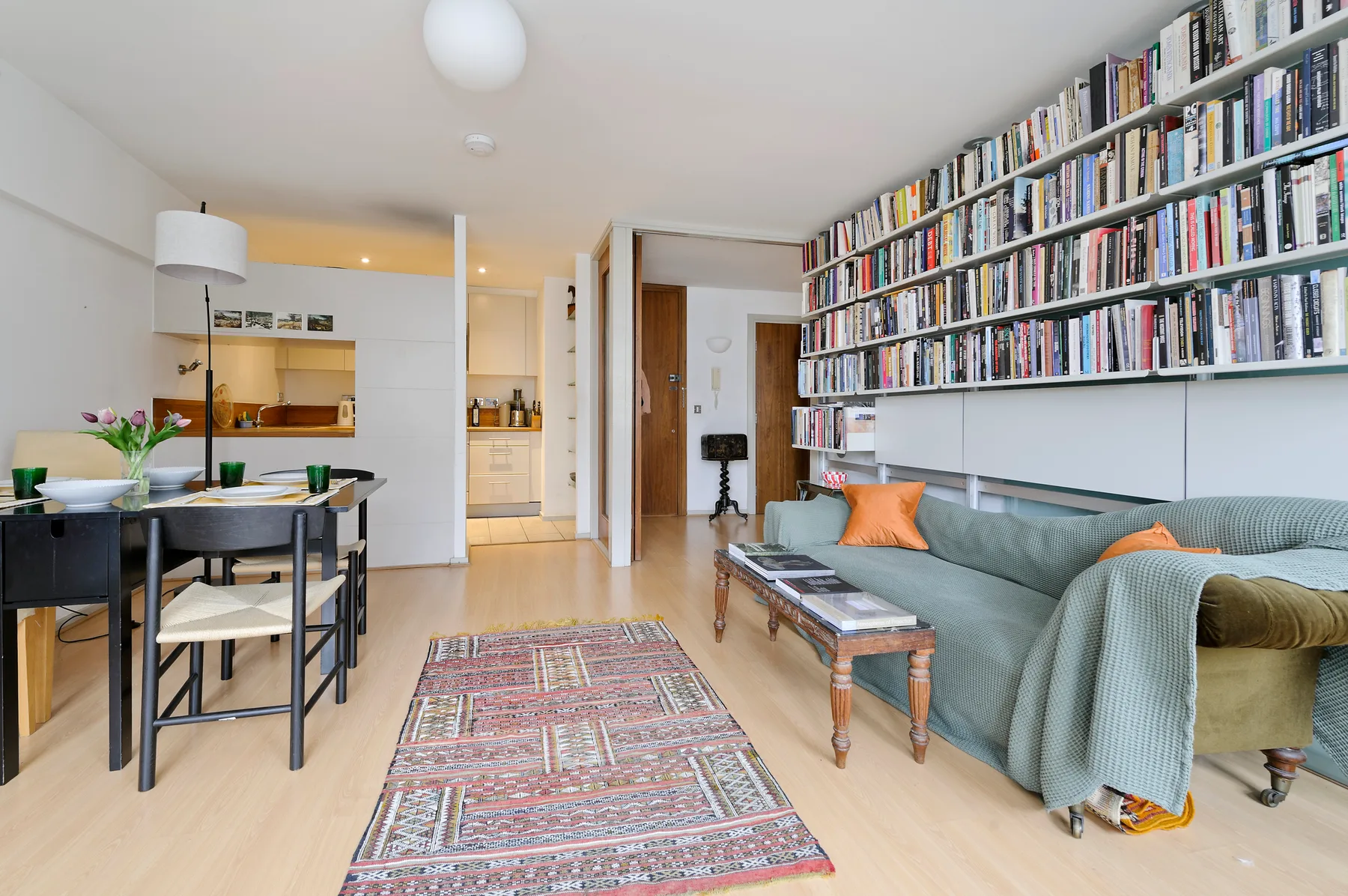 A living room with a long bookshelf above a sofa and a dining table nearby.