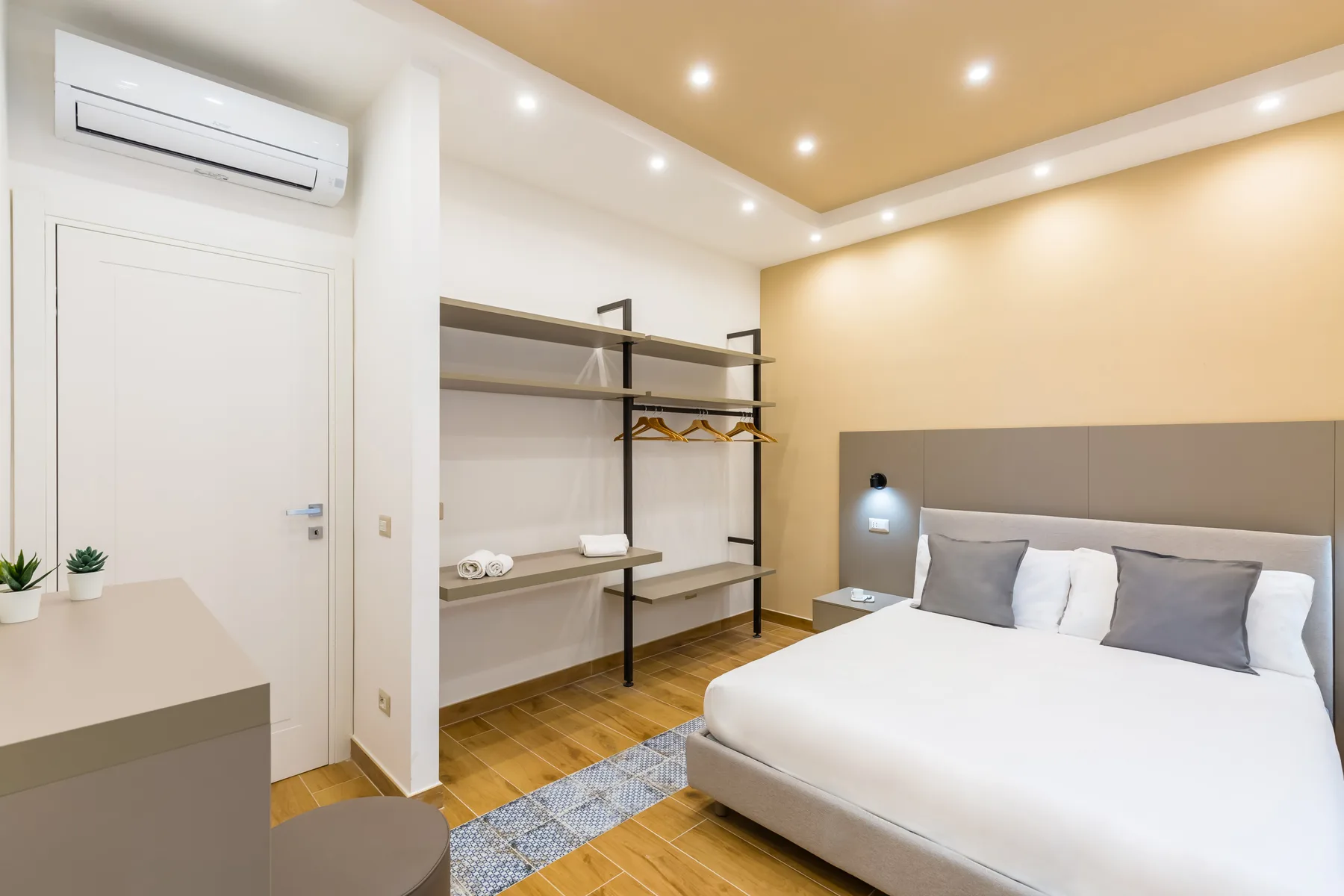 A bright bedroom with a neatly made bed and open shelving along the wall.