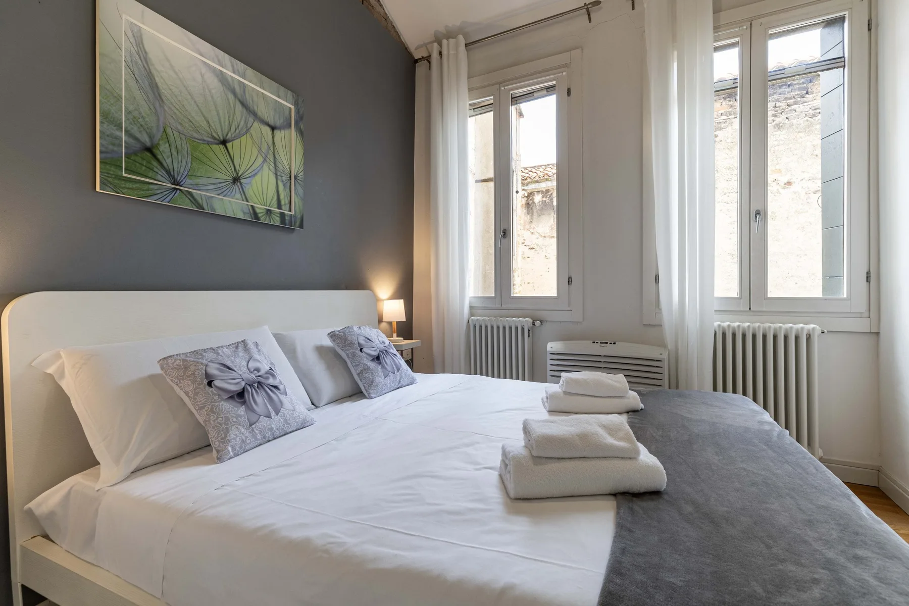 Un dormitorio con una cama bien tendida y ventanas altas.