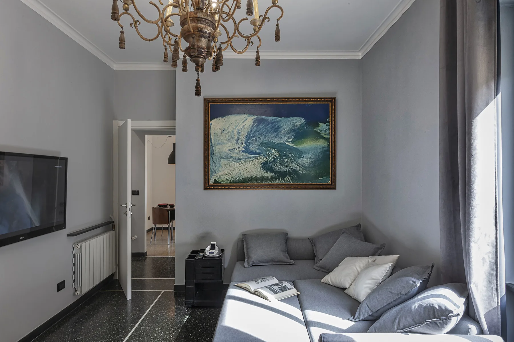 Una sala de estar con asientos grises, un televisor en la pared y una obra enmarcada.