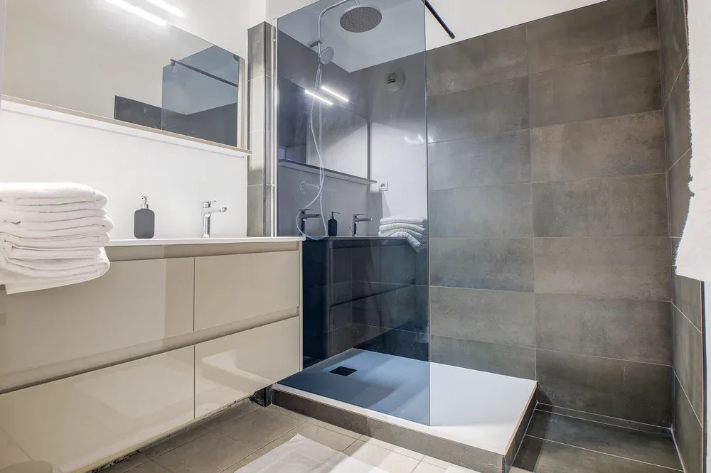A modern bathroom with a glass shower and a vanity topped with folded towels.