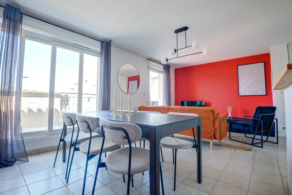 A bright dining and living area with a table, seating, and a red accent wall.