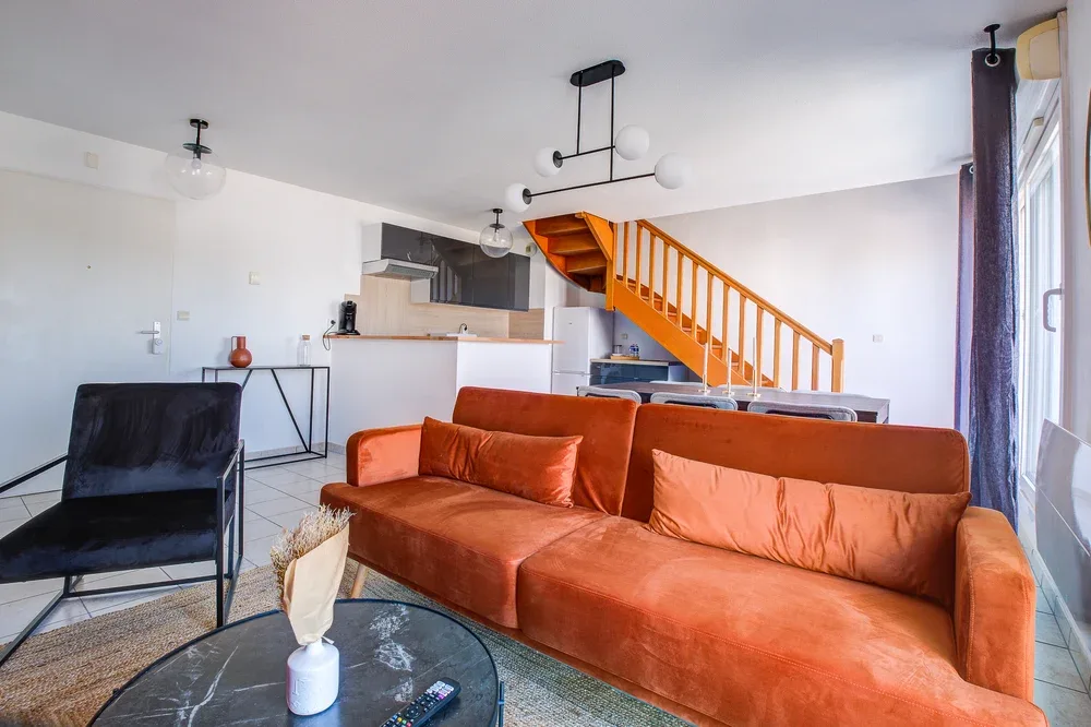 A bright living room with orange seating and an open staircase.