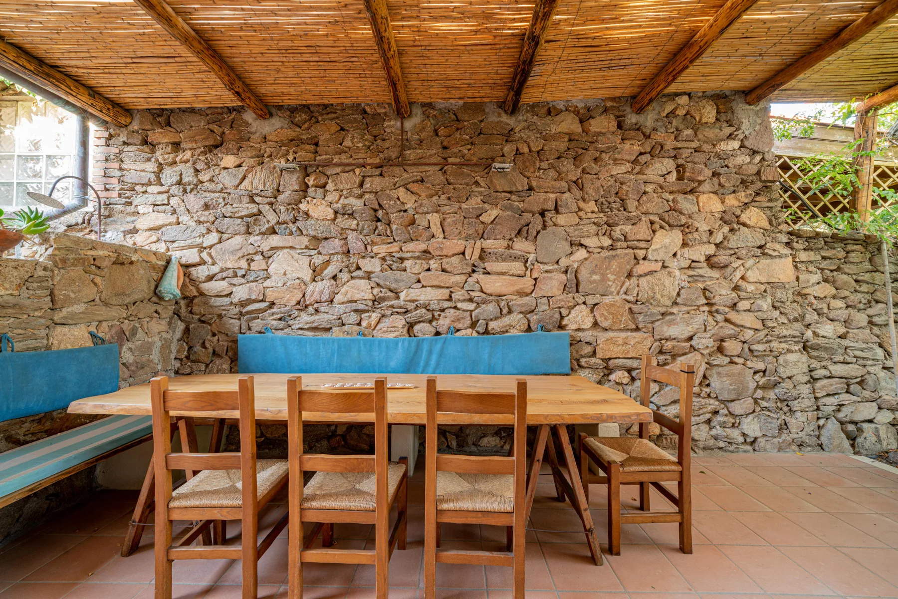 A covered dining area with a wooden table and seating against a stone wall.