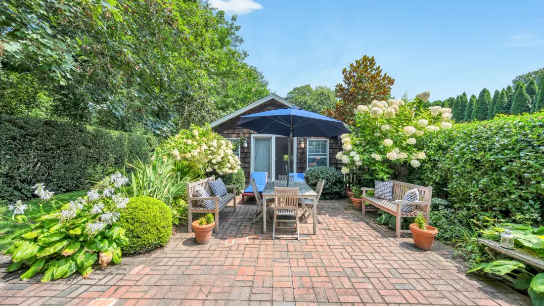 A brick patio with outdoor seating, a table, and a small garden shed.