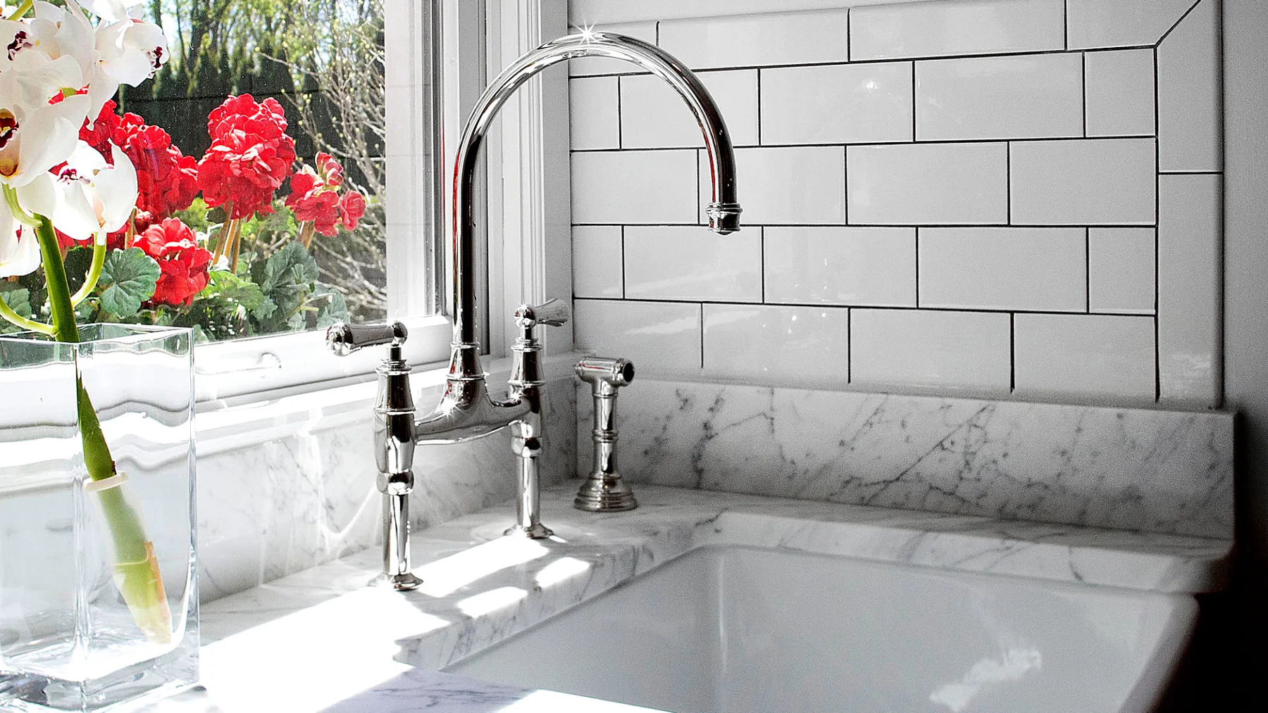 A bright bathroom sink sits beneath a window, with flowers beside it.