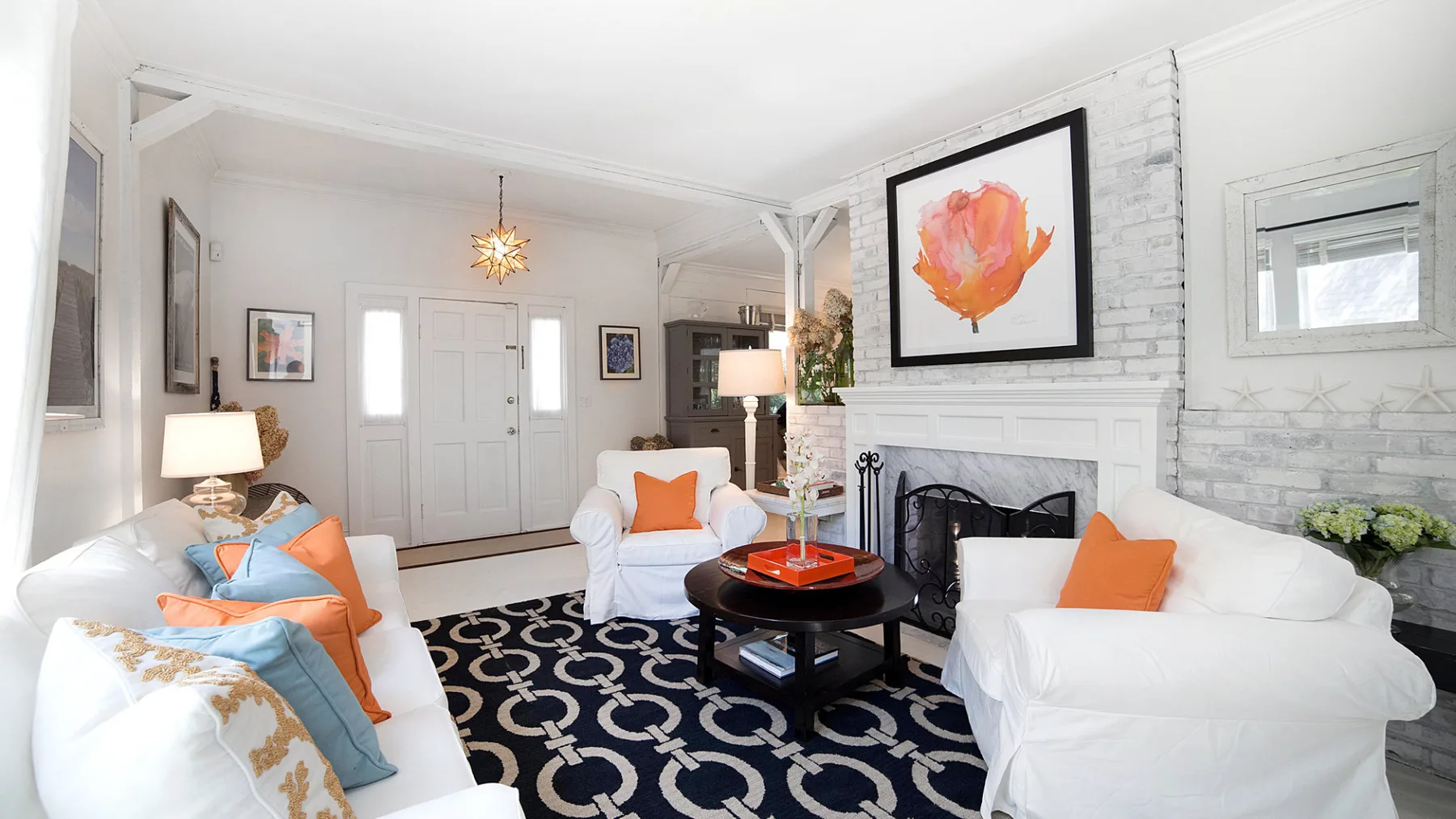 Bright living room with white seating, a fireplace, and a dark patterned rug.