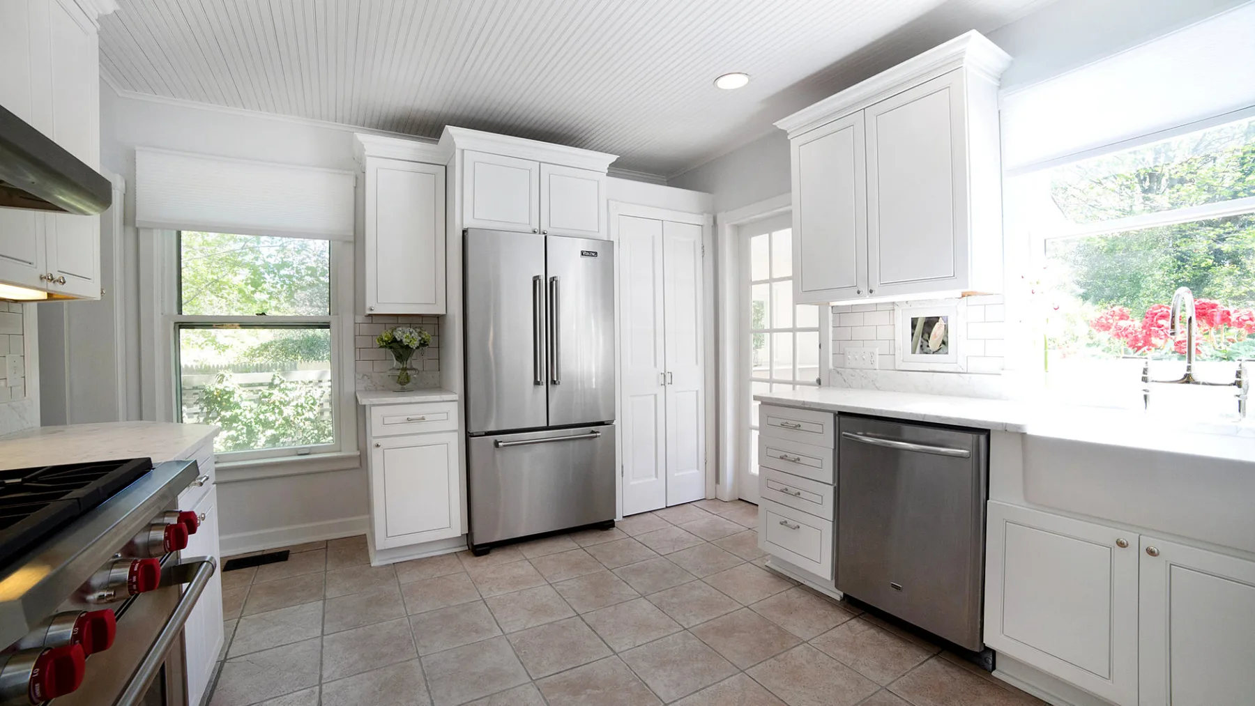 A bright white kitchen with stainless steel appliances and large windows.