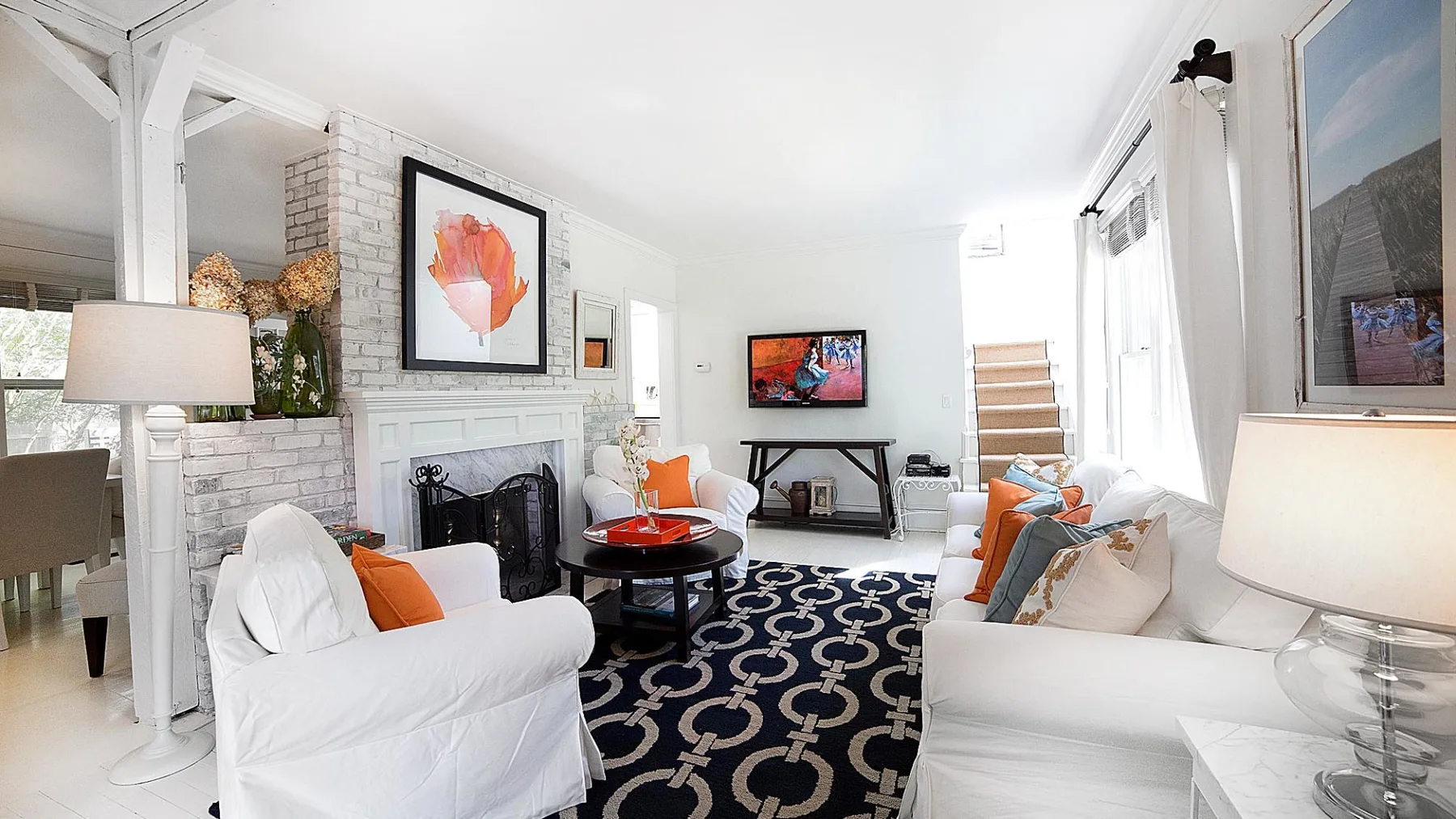 A bright living room has white seating around a black patterned rug and coffee table.