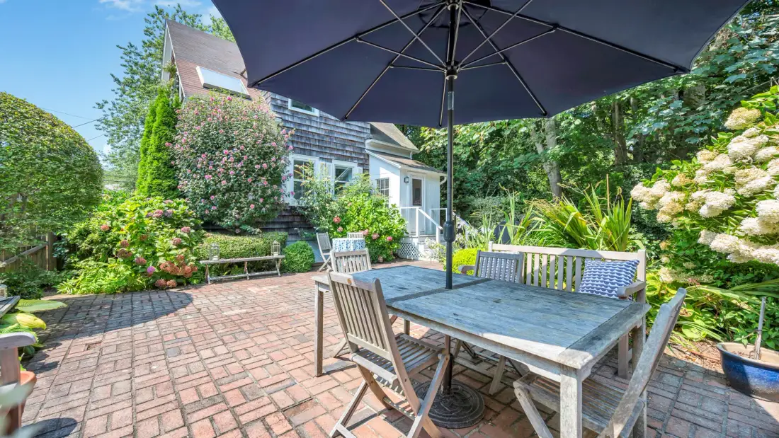 A garden patio has a wooden dining table beneath a large umbrella.
