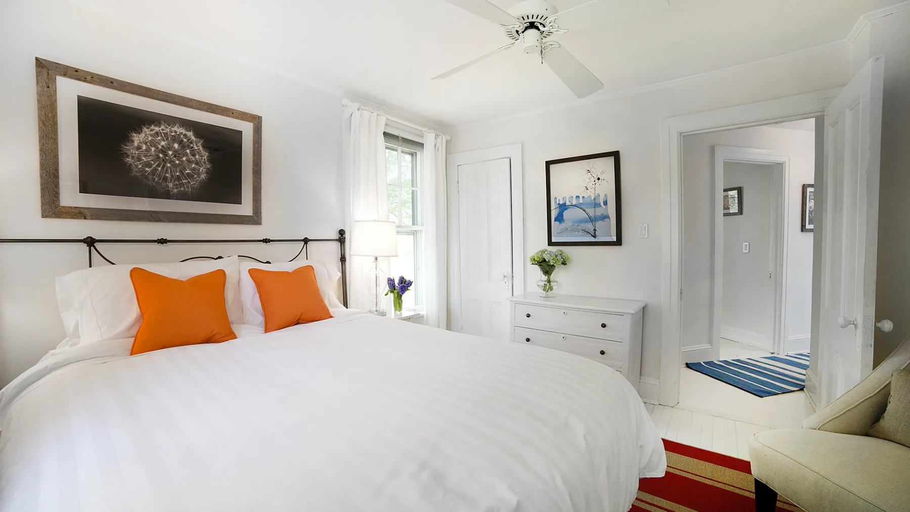 A bright bedroom with a neatly made bed and framed artwork.