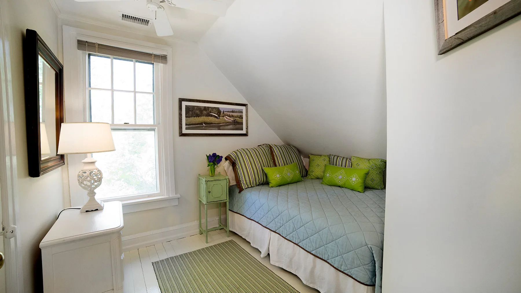 A small bedroom has a bed beneath a sloped ceiling and a window.