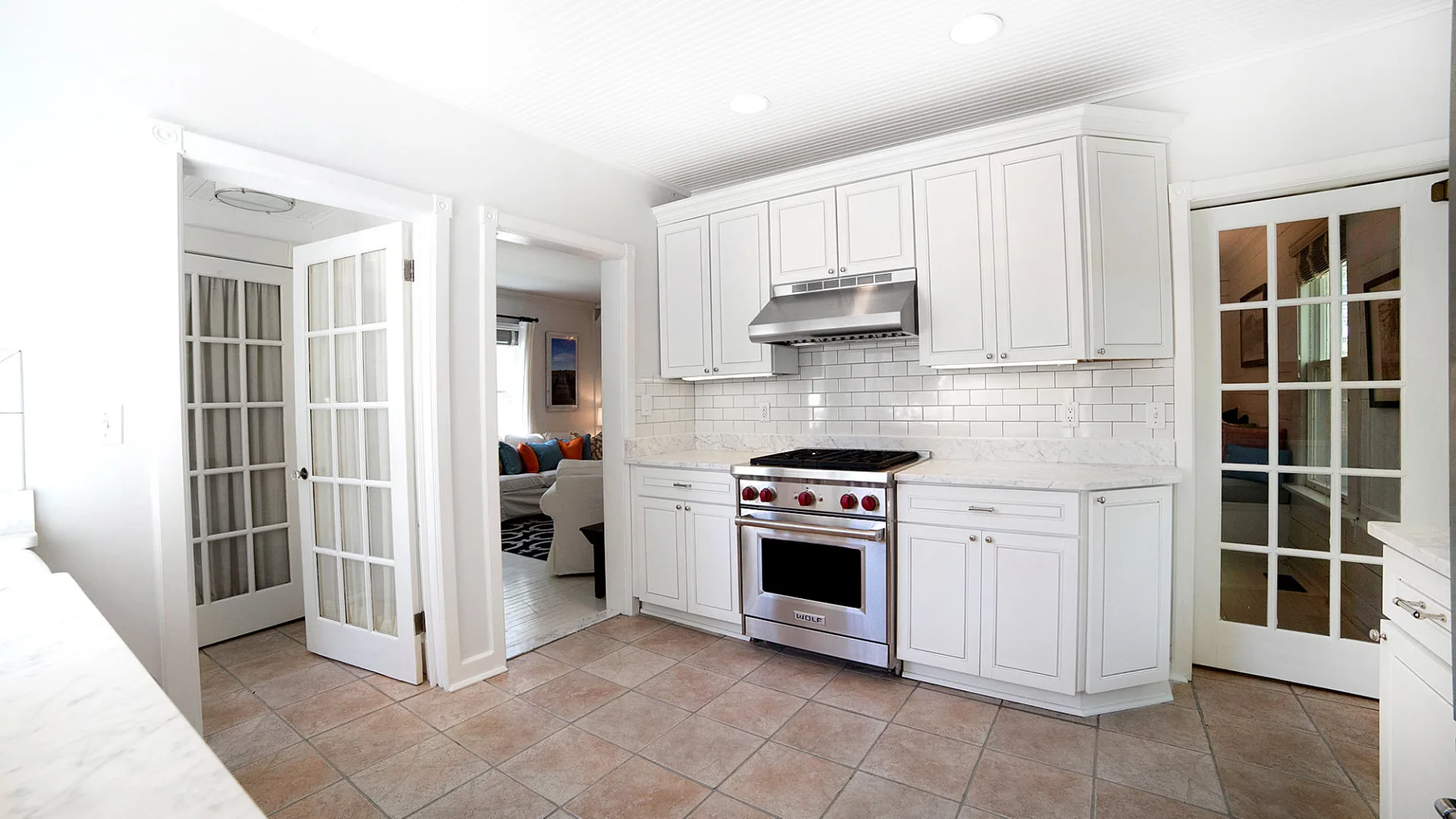 A bright kitchen with white cabinetry, a range, and tiled flooring.