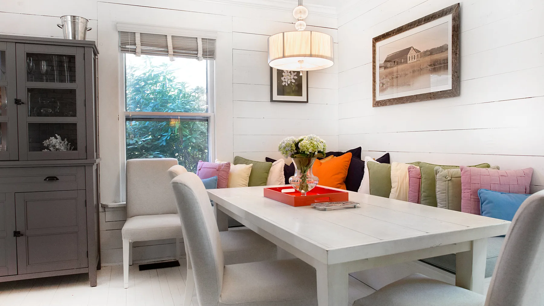 A bright dining area with a long table and cushioned seating along the wall.