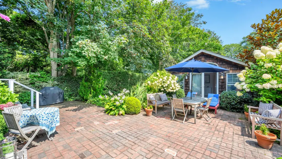 A brick patio with outdoor seating sits beside a small garden shed.