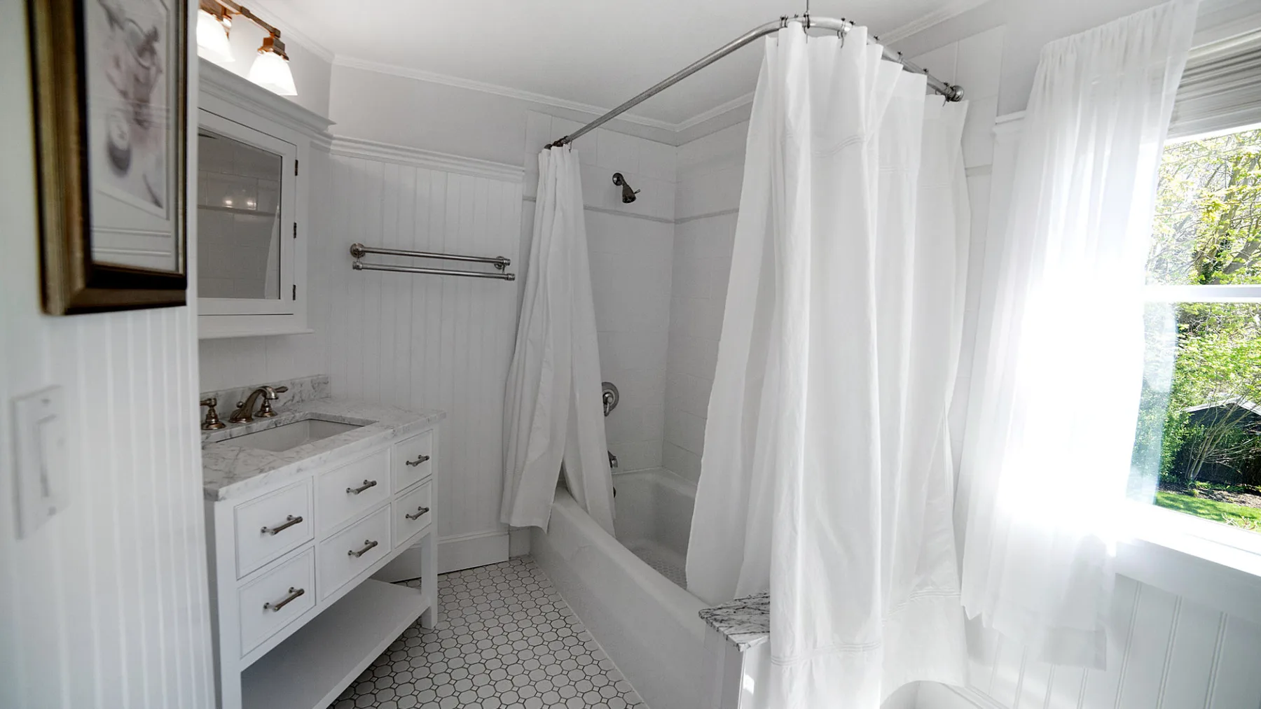 A bright bathroom has a white vanity beside a bathtub with a shower curtain.
