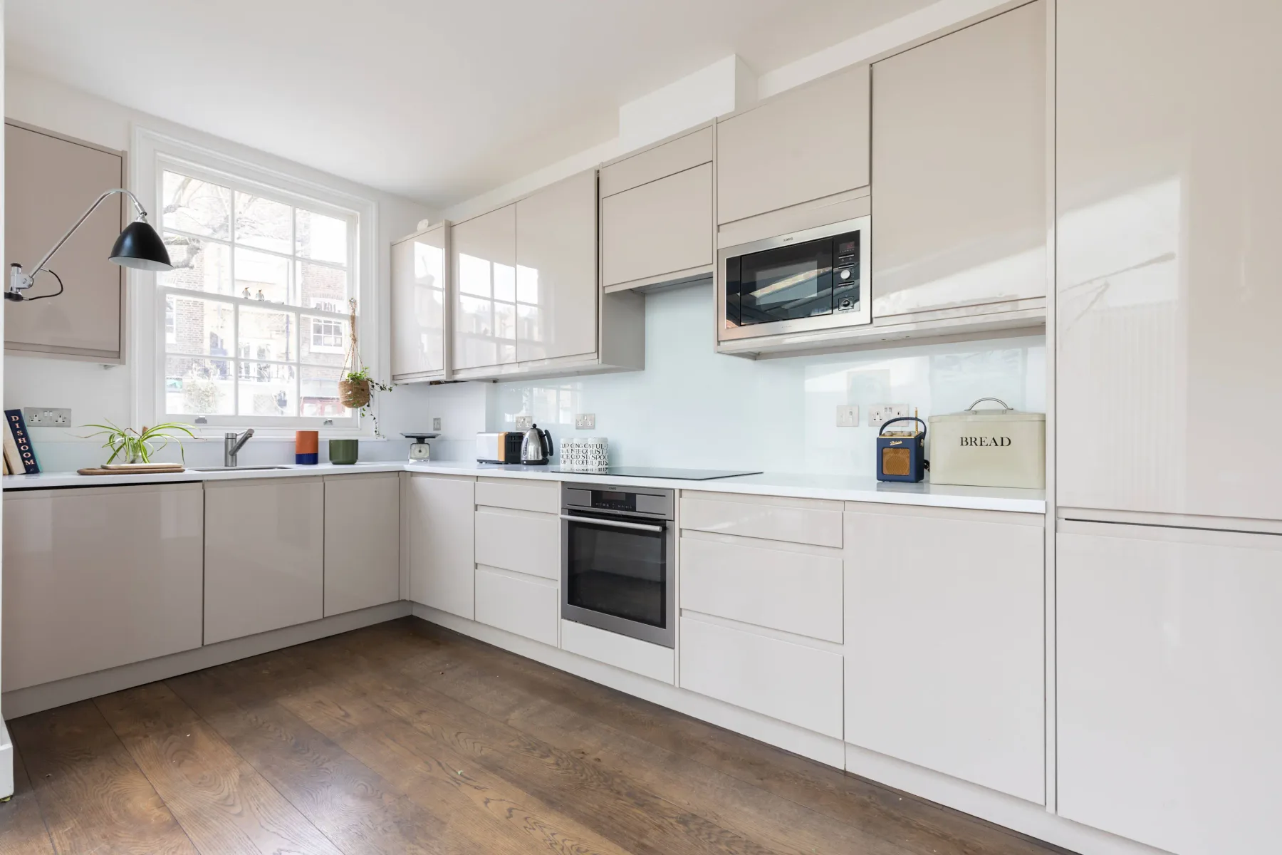 Una cocina luminosa con gabinetes blancos, electrodomésticos integrados y suelo de madera.