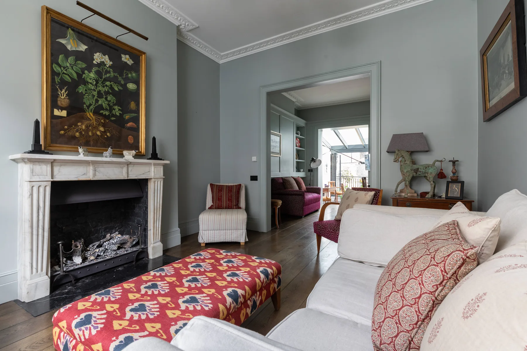 A living room with a fireplace, colorful ottoman, and seating.