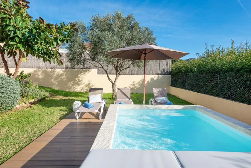 A garden pool beside a wooden deck, with lounge seating and an umbrella.